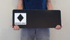 man holding a custom black diamond ski run sign with a black background and white text