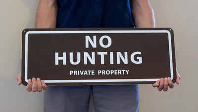 man holding a metal sign with a brown background and white text saying 'no hunting private property'
