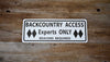 metal sign with black text saying 'backcountry access experts only beacon required' with a white background on a wood background