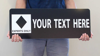 man holding a custom black diamond ski run sign with a black background and white text that says 'your text here'