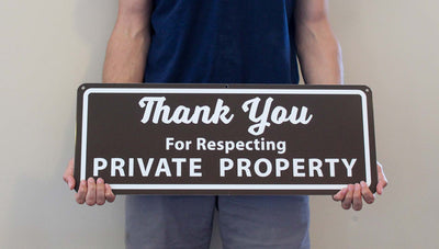 man holding a metal sign that says 'thank you for respecting private property' in white text with a brown background