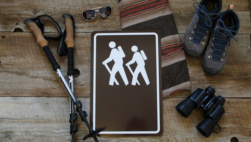 custom hiking trail sign with image of people hiking in white with a brown background and hiking gear around the sign