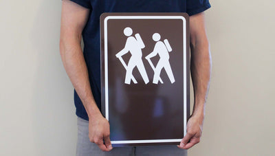 man holding a custom hiking trail sign with image of people hiking in white with a brown background