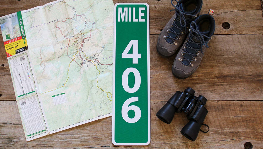 custom metal mile marker sign with a green background and white lettering with travel gear around the sign