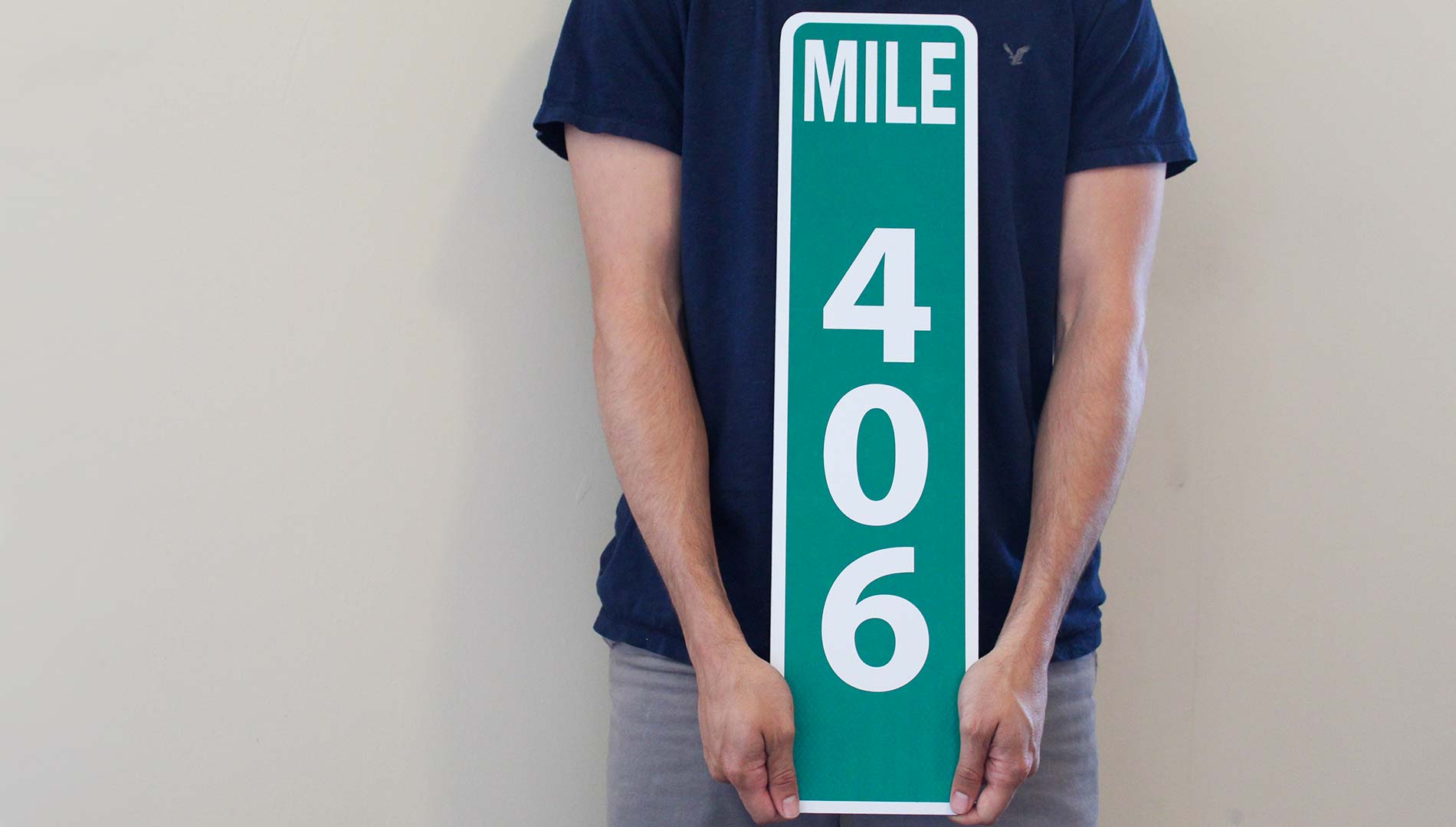 man holding a custom metal mile marker sign with a green background and white lettering