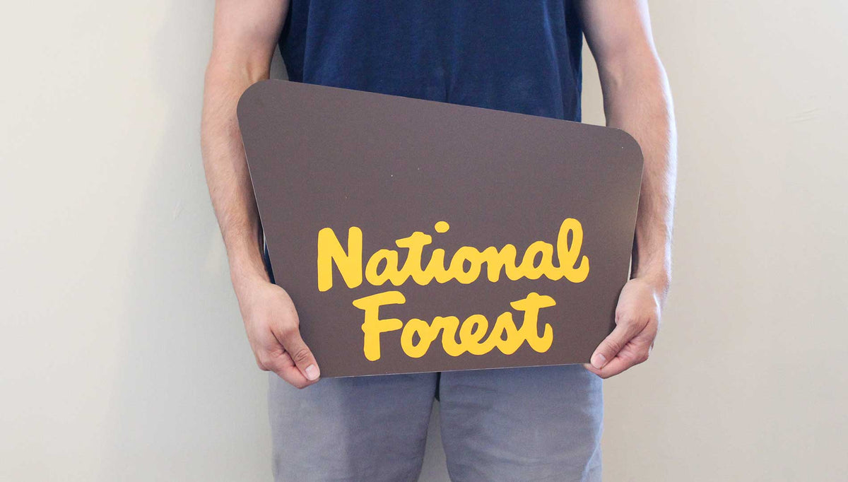 man holding a custom national forest sign with a brown background and yellow text that says 'national forest'