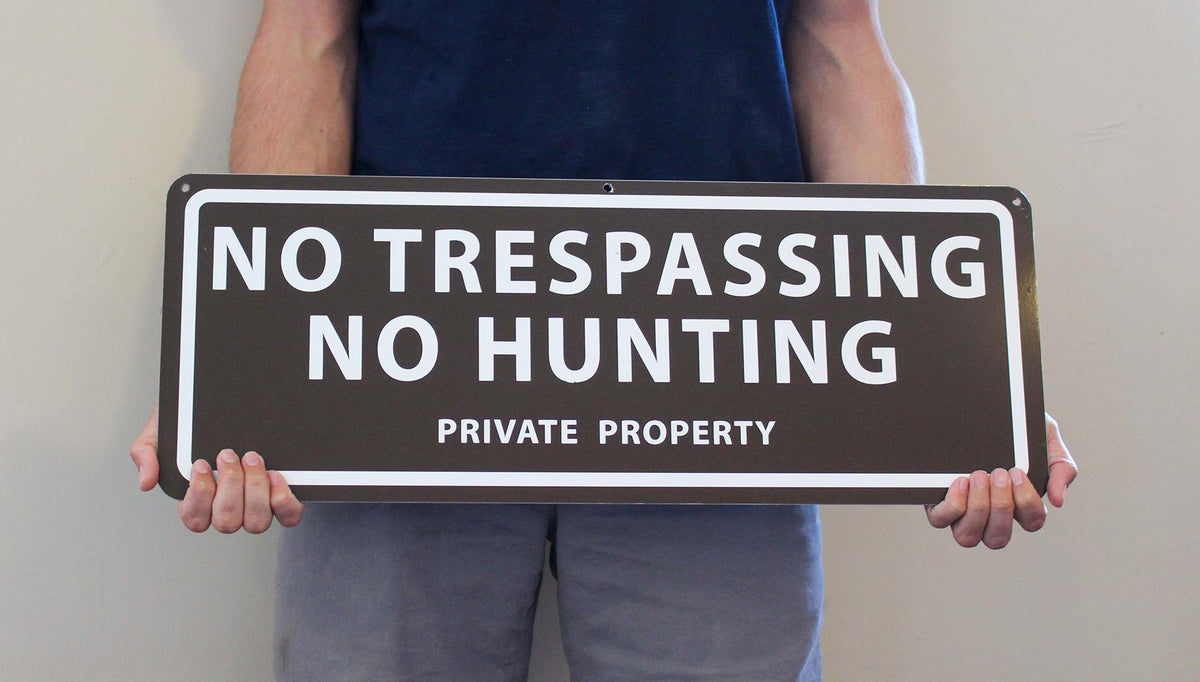 man holding a metal sign with a brown background and white text saying 'no trespassing no hunting private property'