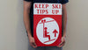 man holding a metal sign with a white background and red text that says 'Keep Ski Tips Up' with an image of a skier on a chairlift