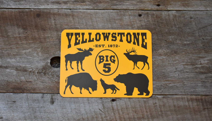 metal sign with a yellow background and black text that says 'Yellowstone Big 5' with black outlines of a moose, elk, bison, wolf, and grizzly bear with antlers and pine needles and cones around it