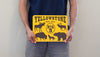 man holding a metal sign with a yellow background and black text that says 'Yellowstone Big 5' with black outlines of a moose, elk, bison, wolf, and grizzly bear