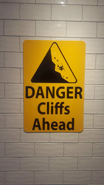 metal sign with black text saying 'danger cliffs ahead' with a yellow background and image of falling rock