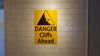 metal sign with black text saying 'danger cliffs ahead' with a yellow background and image of falling rock