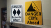 metal sign with black text saying 'danger cliffs ahead' with a yellow background and image of falling rock on a mantle