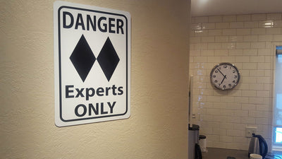 metal sign with black text saying 'danger experts only' with a two black diamonds on a white background