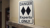 angled photo of a metal sign with black text saying 'danger experts only' with a two black diamonds on a white background