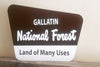 brown and white metal sign with text saying 'gallatin national forest land of many uses'
