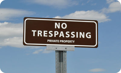 metal sign with white text saying 'no trespassing private property' with a brown background