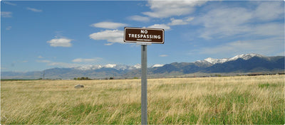 metal sign with white text saying 'no trespassing private property' with a brown background on a post
