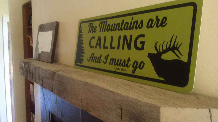metal sign with a yellow background and black text saying 'the mountains are calling and i must go' on a mantle